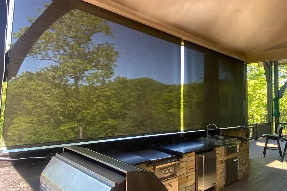 Outdoor covered kitchen with black countertop and mesh shades overlooking a green hillside