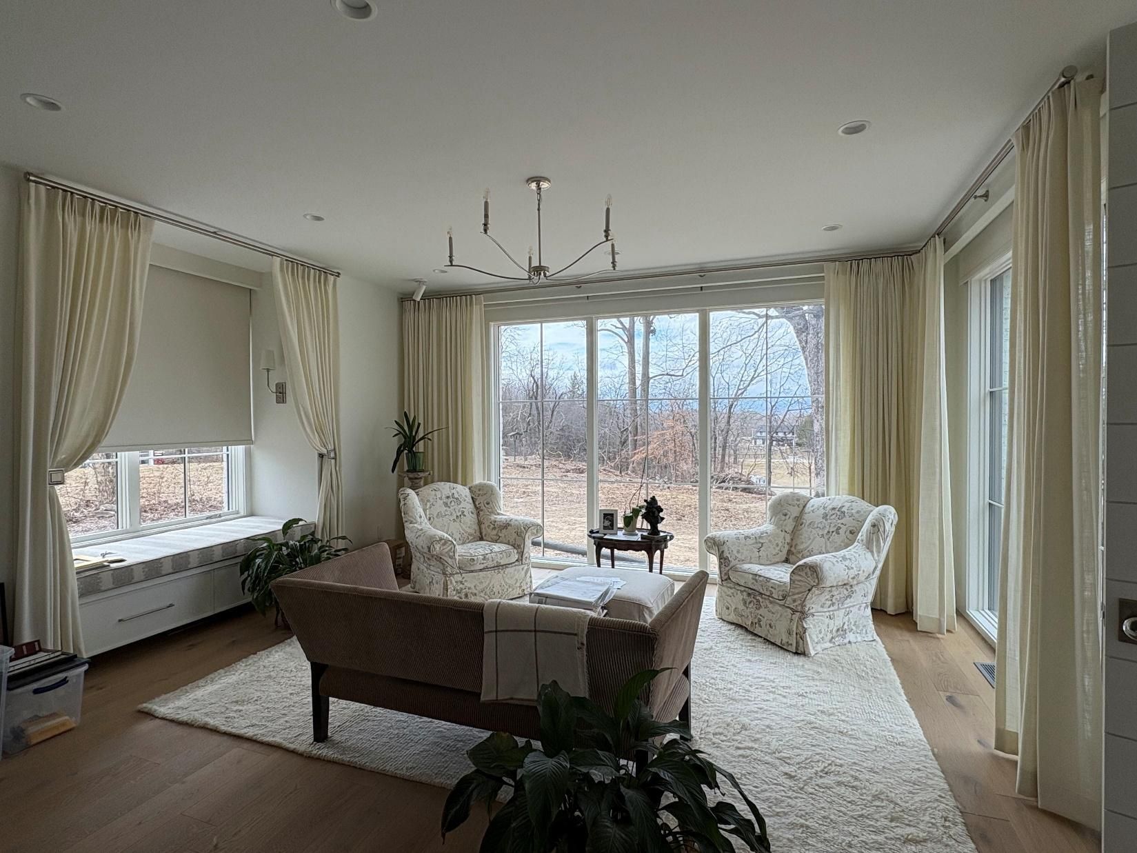 Bright living room with cream curtains, large windows, white rug, and beige sofas around a coffee table.