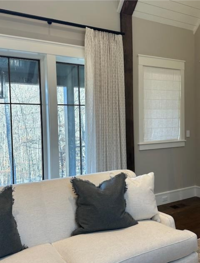 Modern living room with gray sofa, dark pillows, window curtains, and white blinds