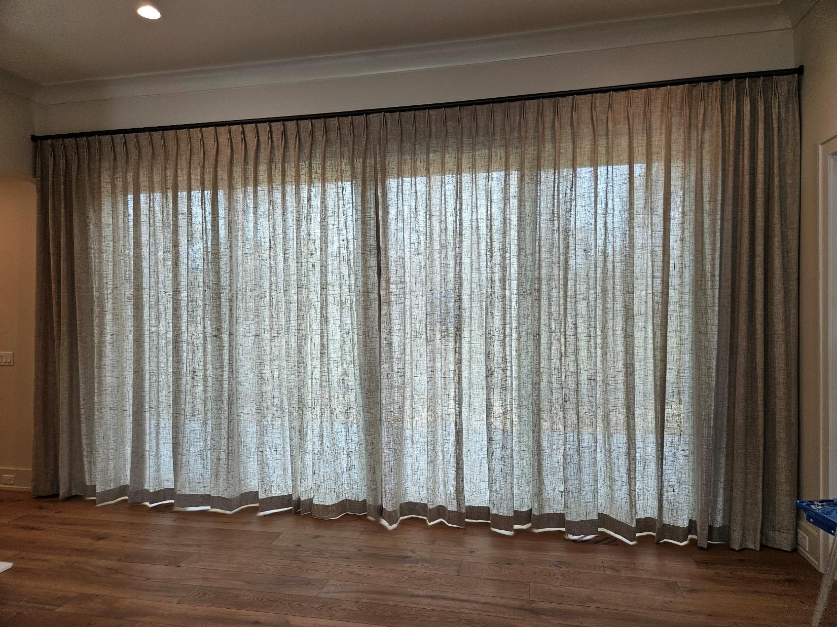 Floor-to-ceiling sheer curtains covering a large window in a wood-floored room.
