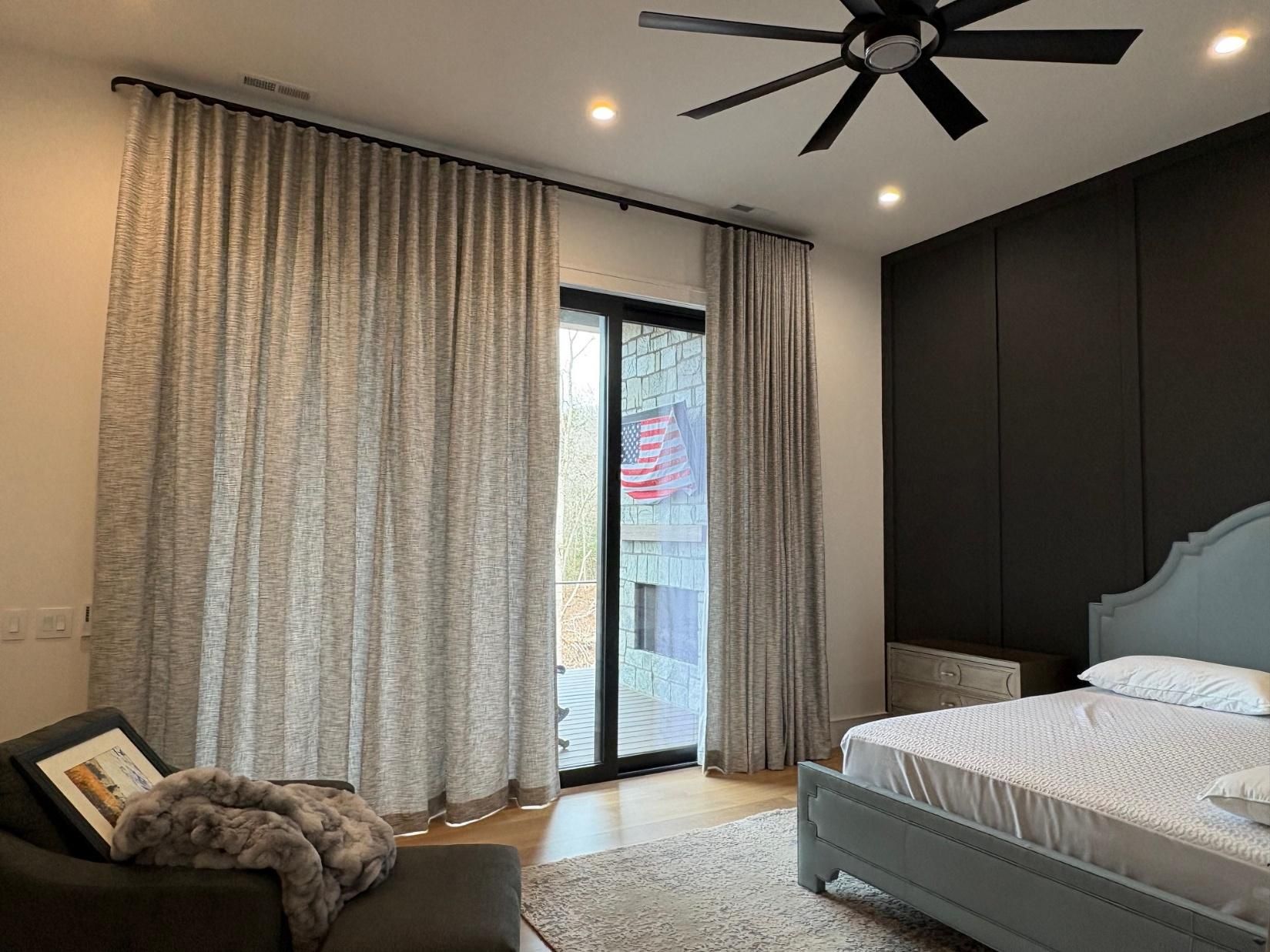 Modern bedroom with a bed, black ceiling fan, floor-to-ceiling curtains, and glass door to a balcony.