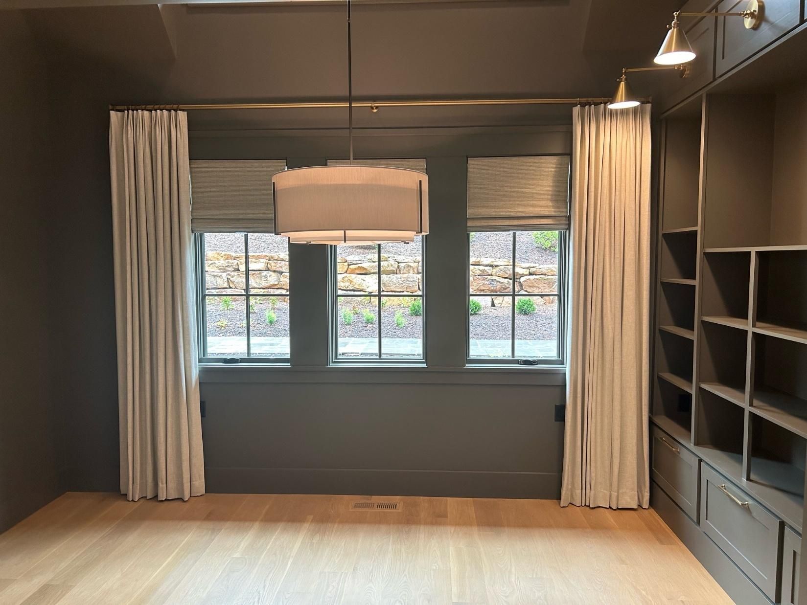 Empty modern room with dark walls, wood floor, windows with curtains, and built-in shelving