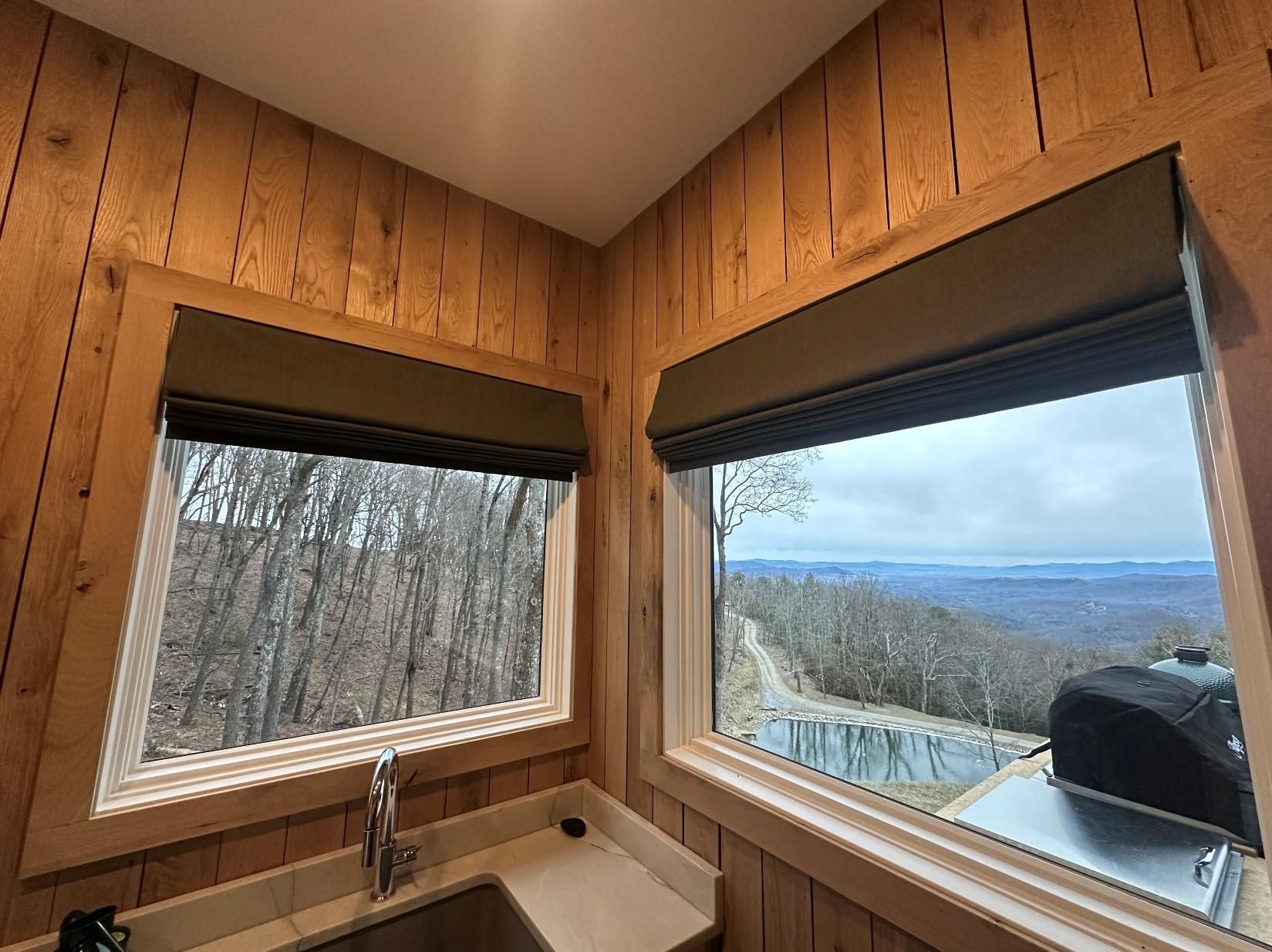 Wood-paneled corner with two windows overlooking a forest and distant hills