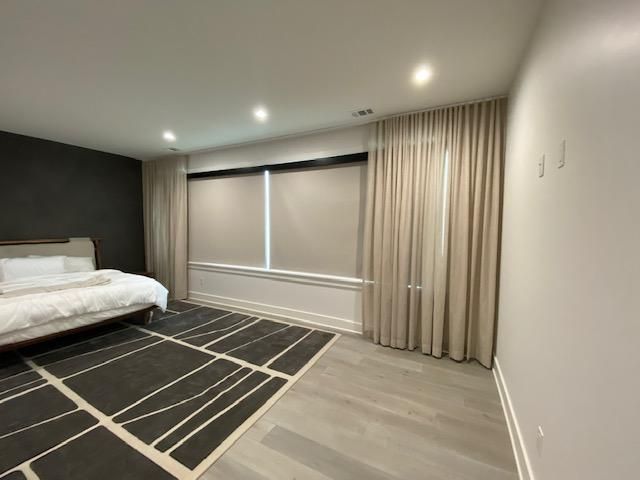 Spacious modern bedroom with a bed, black accent wall, striped rug, and beige curtains over a window