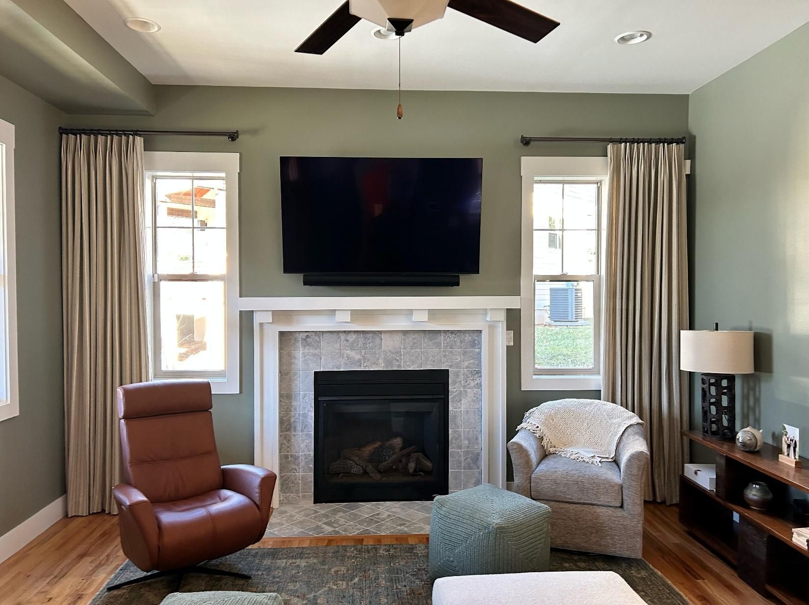 Living room with fireplace, wall-mounted TV, two chairs, and neutral decor in daylight