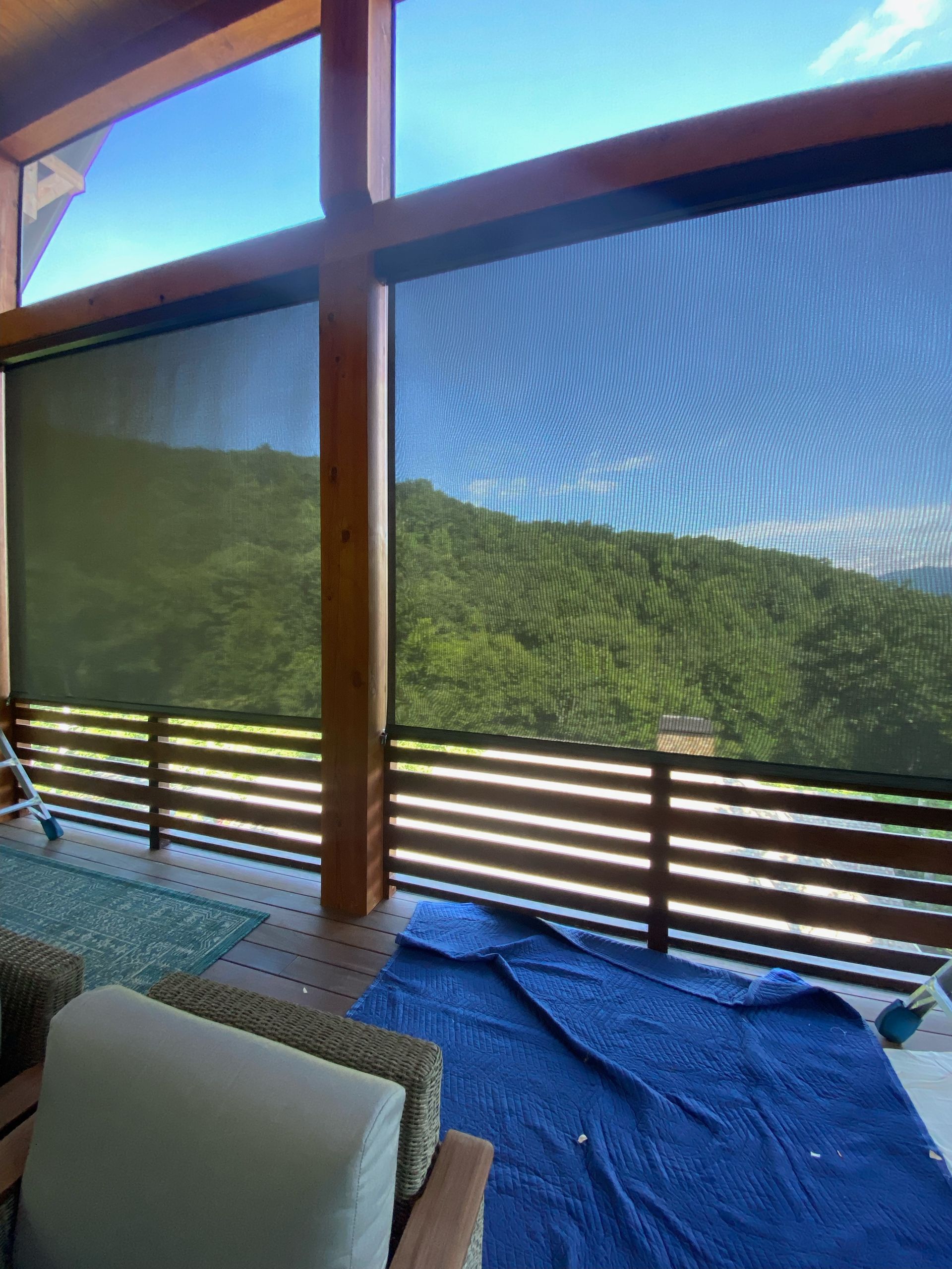 Covered balcony with mesh screens, mountain view, chair, and blue tarp on the floor.