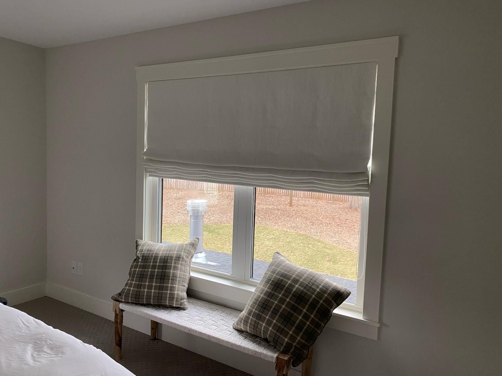 White window seat with gray blinds and two plaid pillows in a bright room