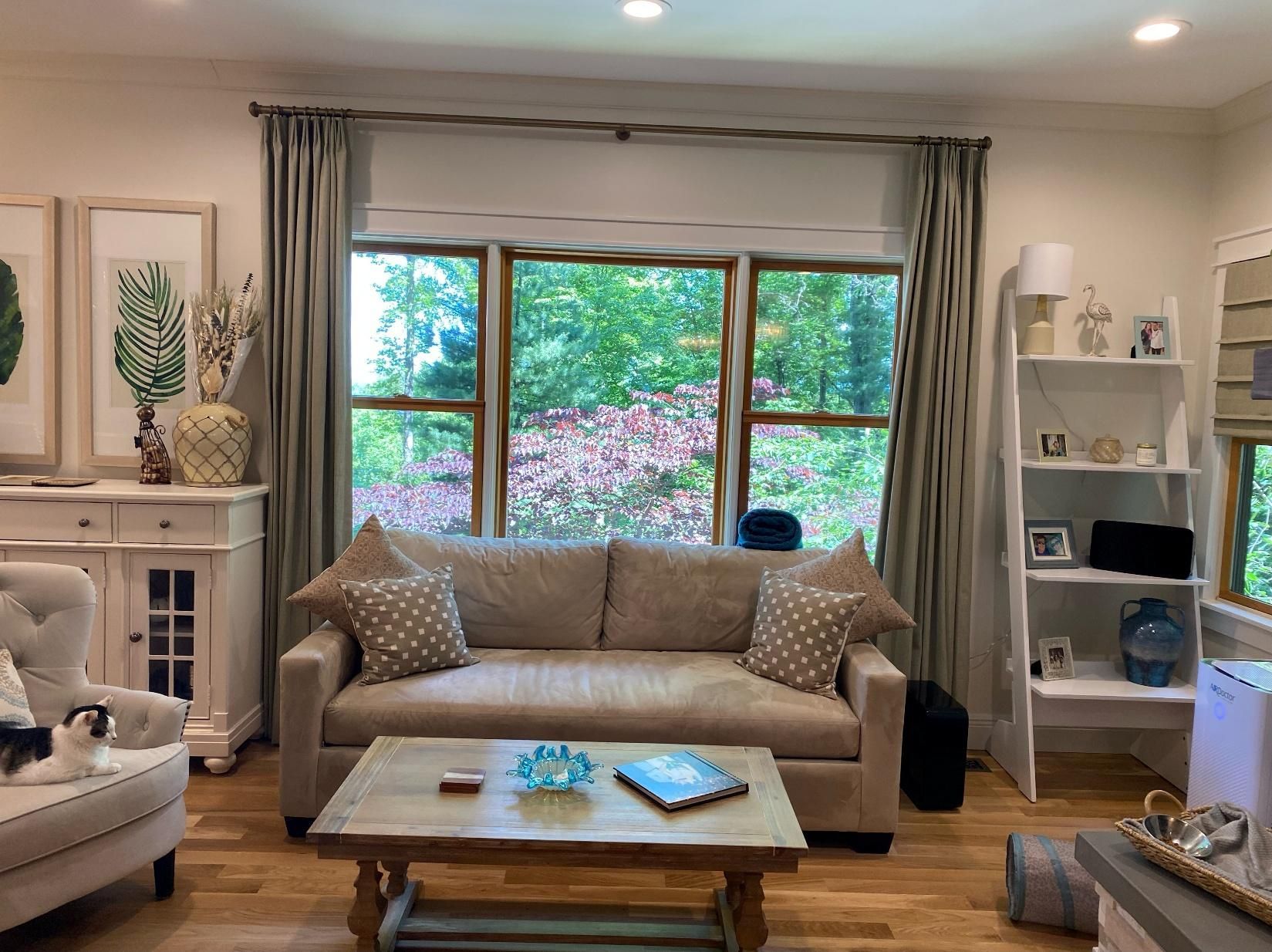 Bright living room with beige sofa, coffee table, large window, and white shelving units
