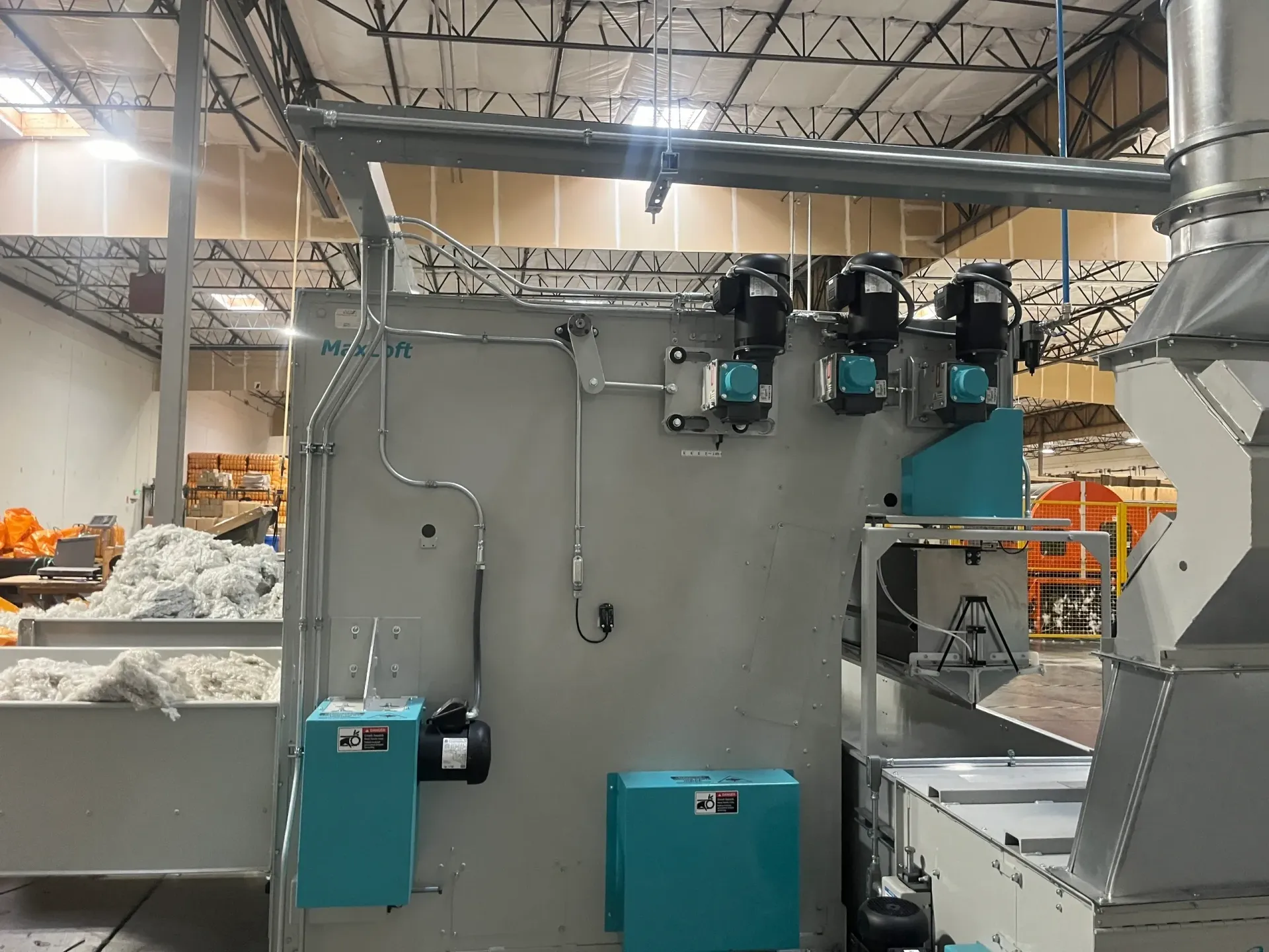 Industrial machinery with turquoise and gray components in a factory setting, with piping and ventilation.