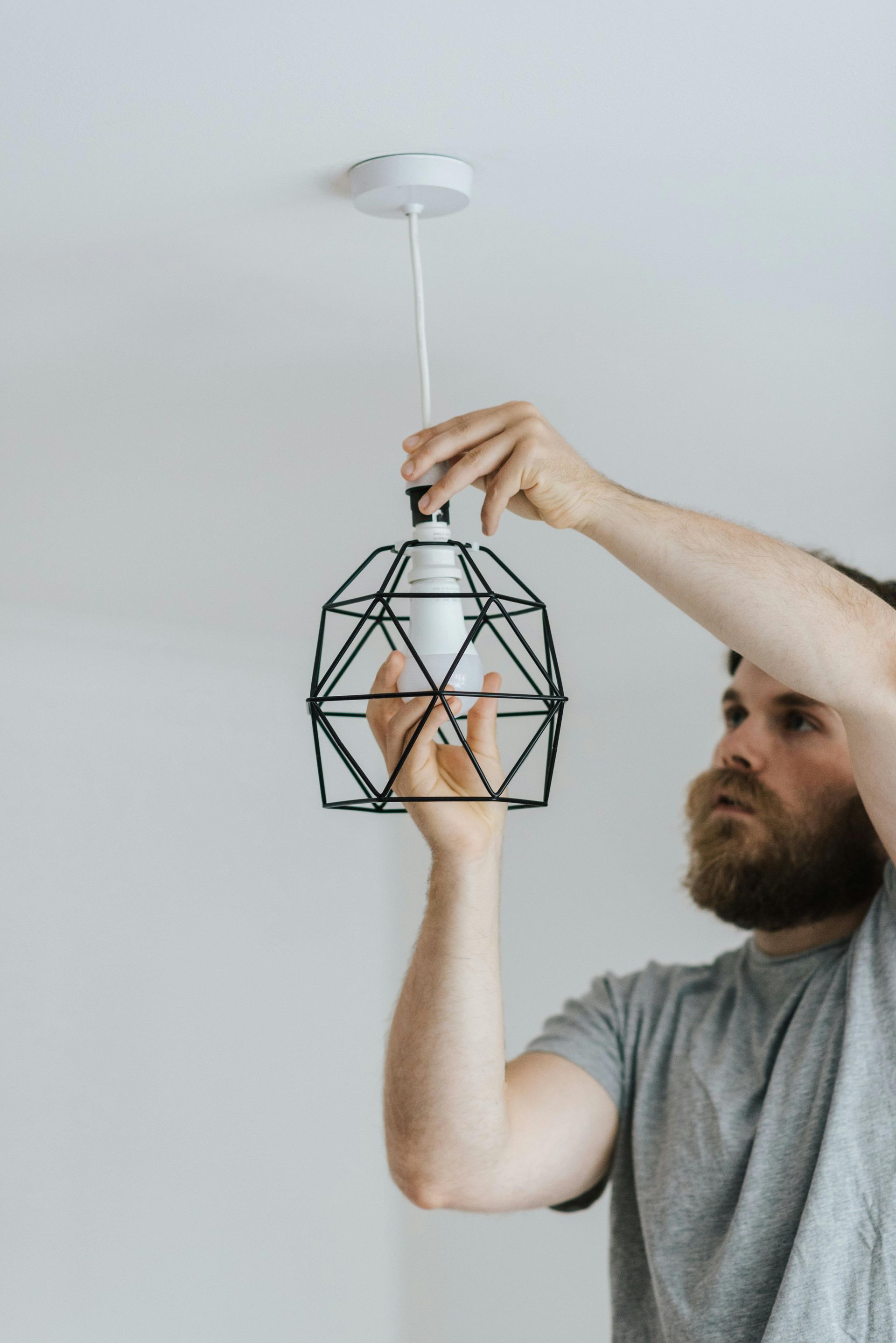 Man installs a black wireframe pendant light fixture on a white ceiling.