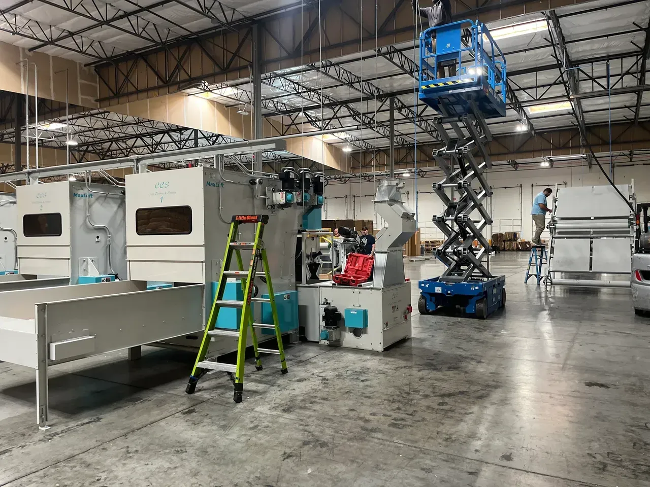 Workers on lifts installing machinery inside a warehouse.
