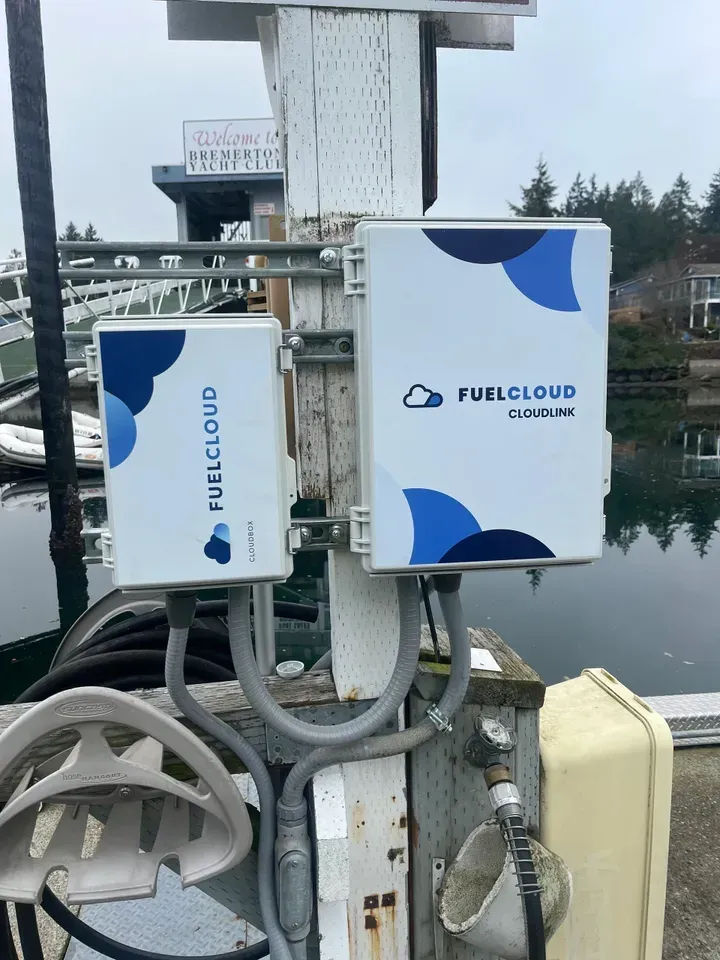 Two white FuelCloud boxes mounted on a pier, near a fuel pump, with a cloudy logo.