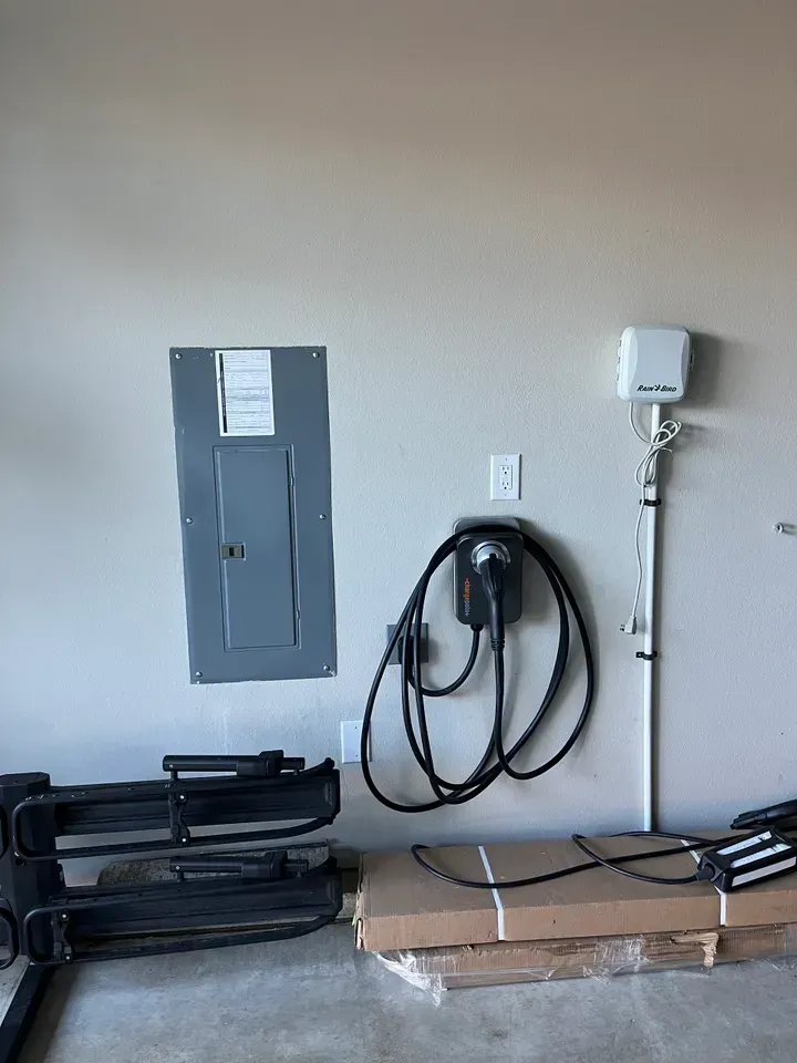 Electric vehicle charger and electrical panel on a garage wall.