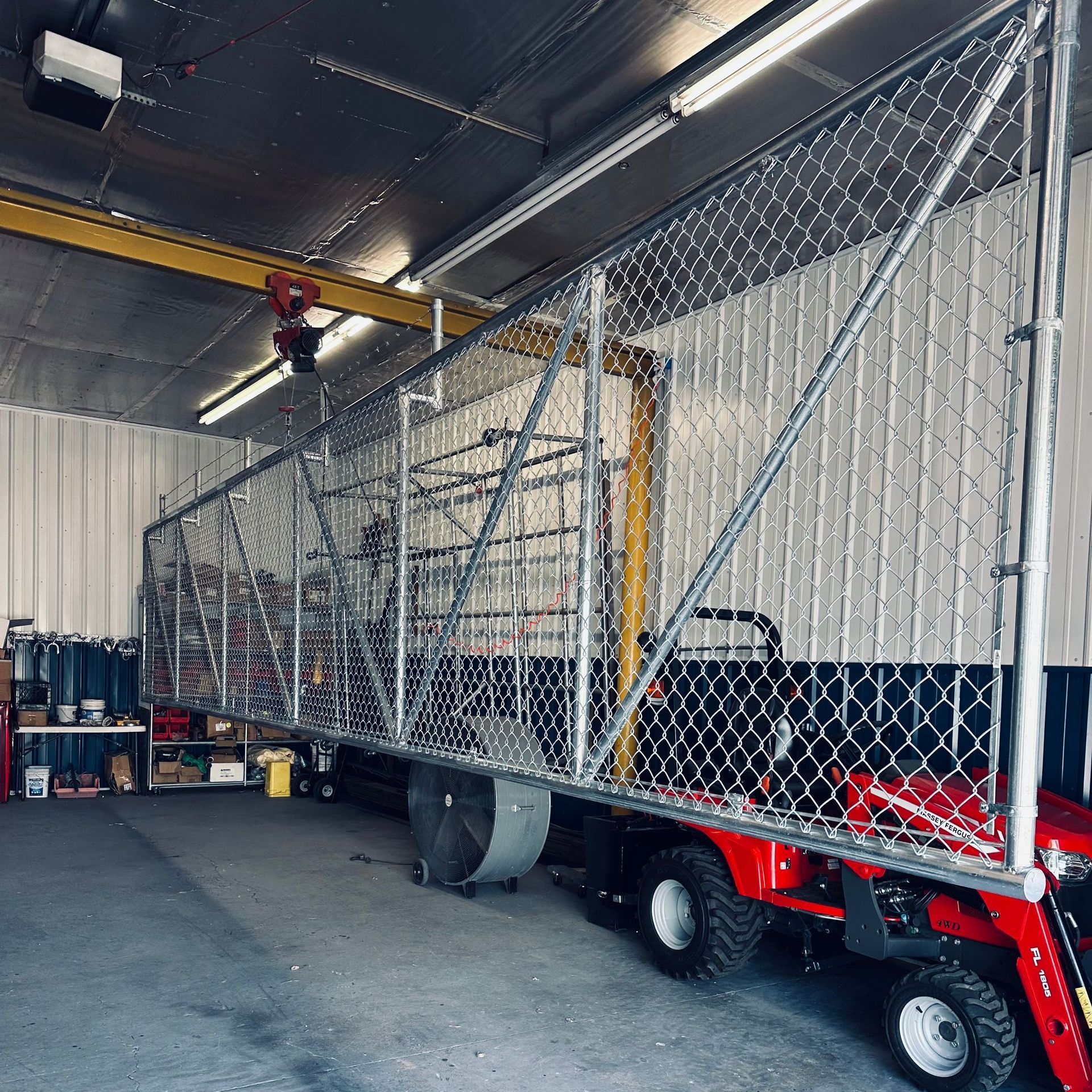 A red snow blower is parked in a garage behind a chain link fence