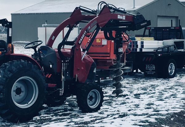 A red tractor with a drill attached to it is parked in front of a building.