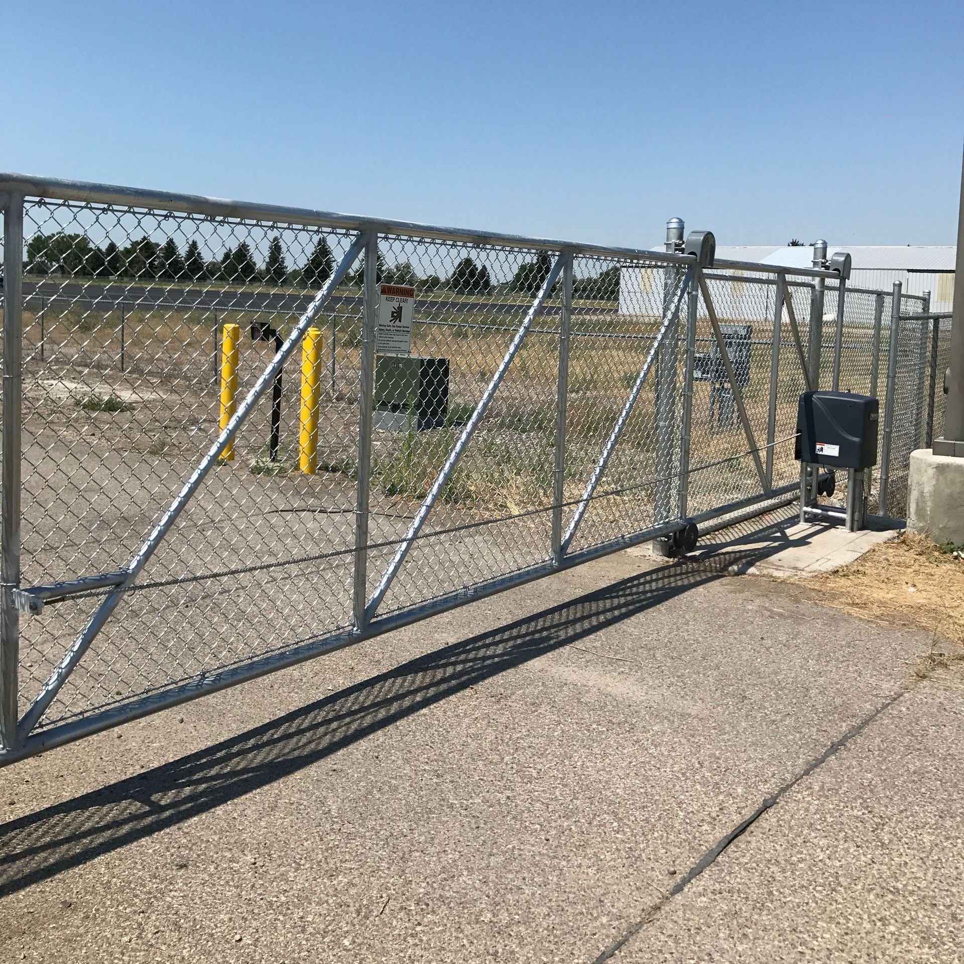 A chain link fence with a gate and a shadow on the sidewalk.