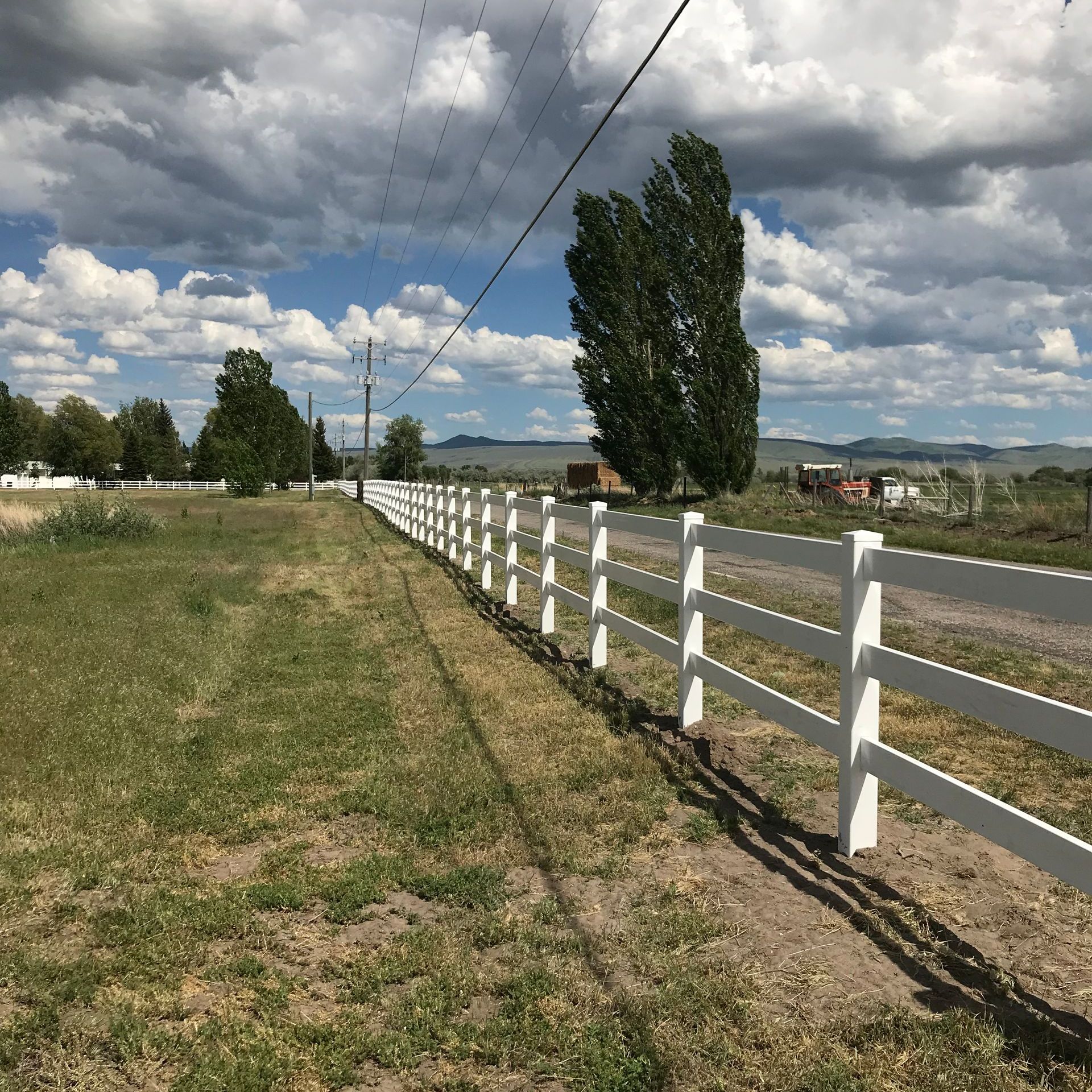 A white fence surrounds a grassy field on a cloudy day
