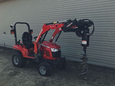A red tractor with a drill attached to it is parked in front of a building.