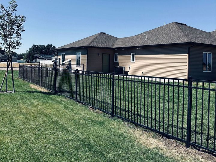A black fence surrounds a lush green yard in front of a house.