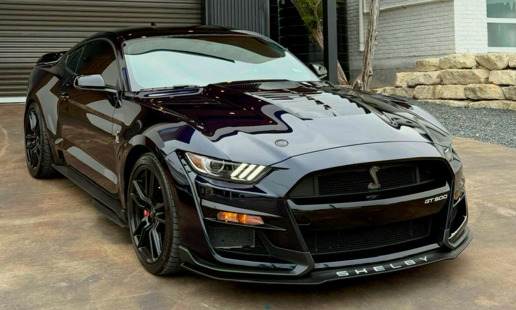 Dark purple Ford Mustang Shelby GT500 sports car parked in front of a building.