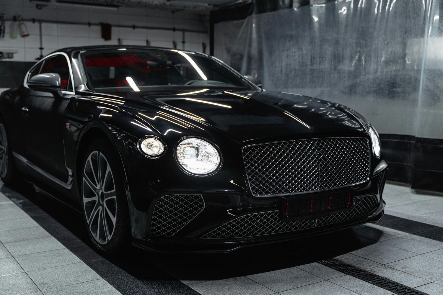 Black luxury car parked indoors in a dim garage, front view with headlights on