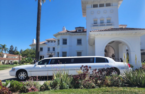 A white limousine is parked in front of a large white building.