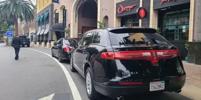 A black car is parked on the side of the road in front of a building.