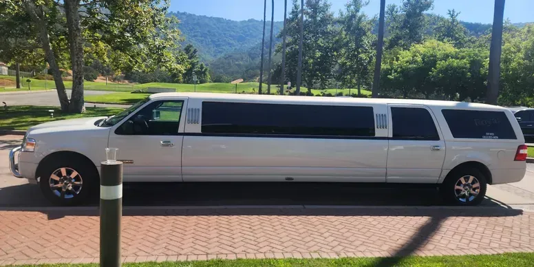 A white limousine is parked in a parking lot next to a golf course.