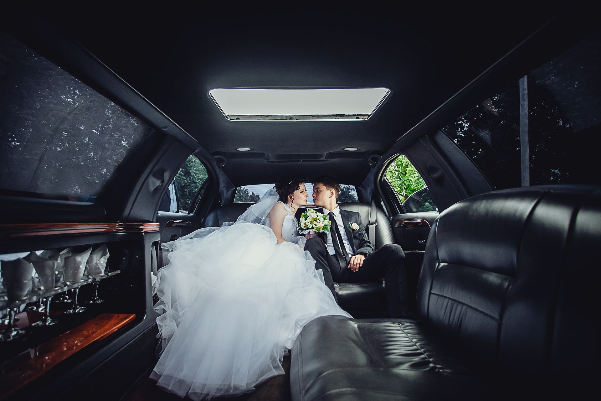 A bride and groom are kissing in the back of a limousine.