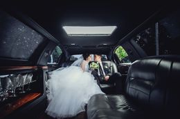 A bride and groom are kissing in the back of a limousine.