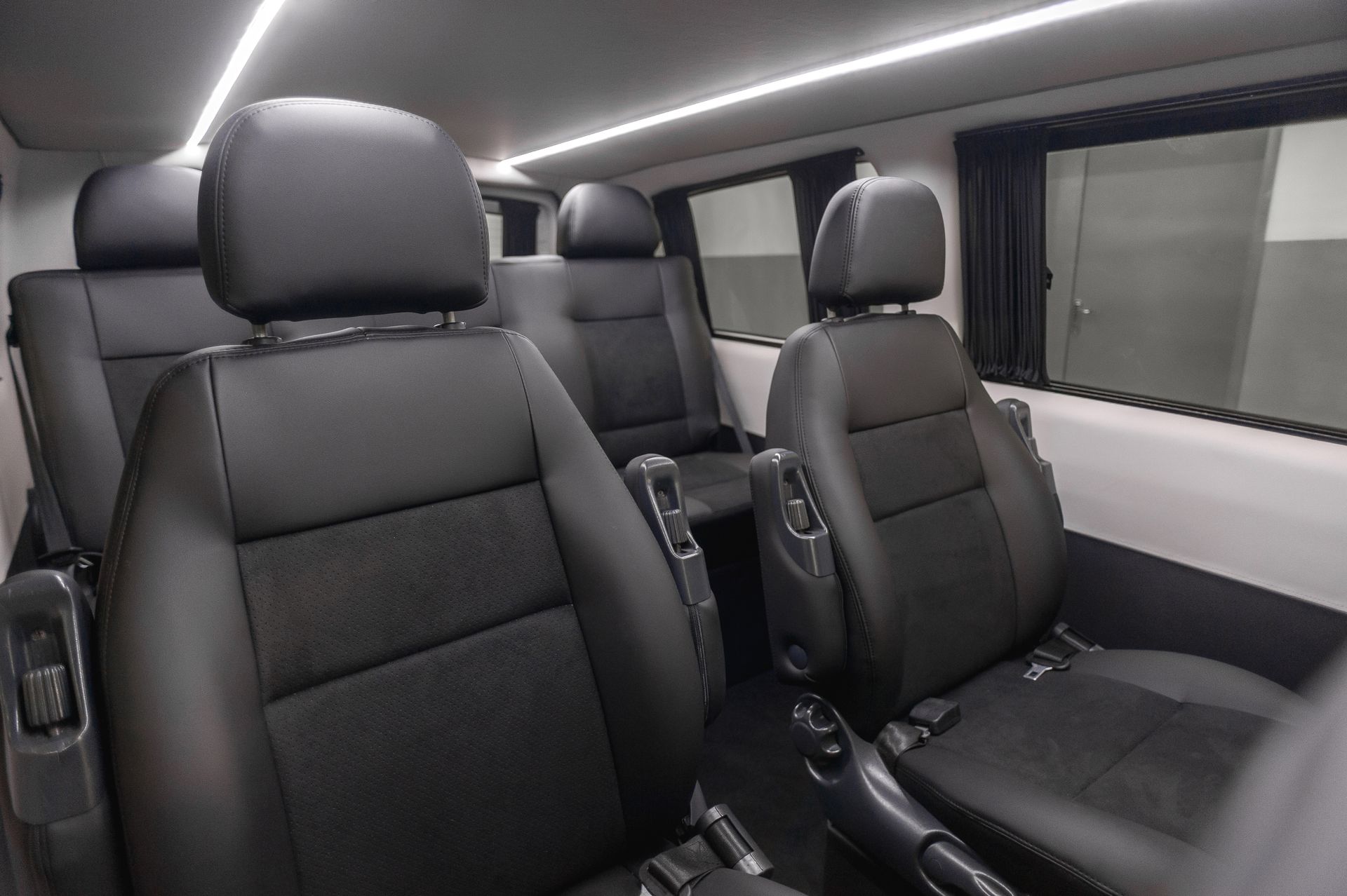The interior of a van with black leather seats and a lot of windows.