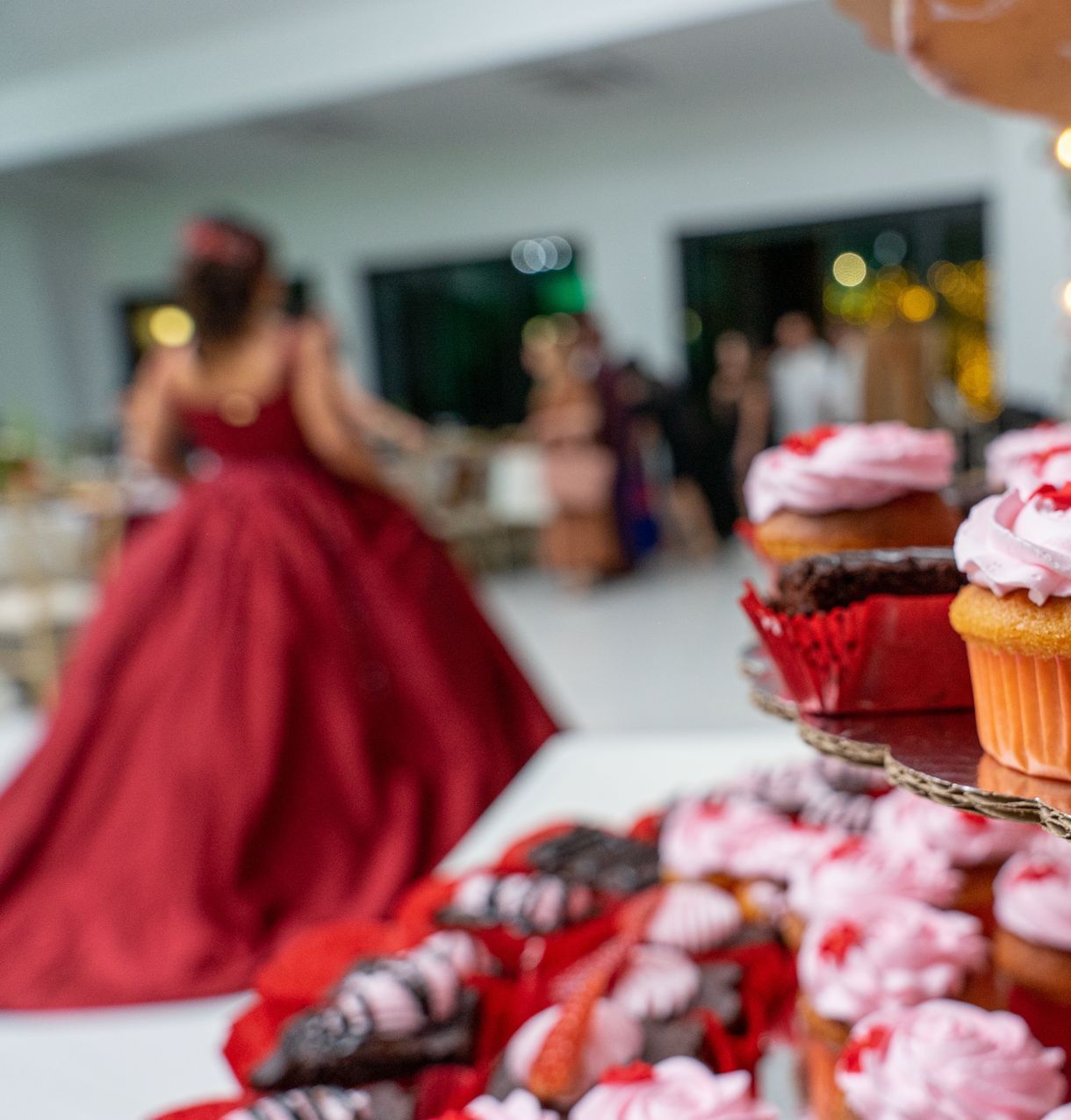 A woman in a red dress is standing behind a display of cupcakes.