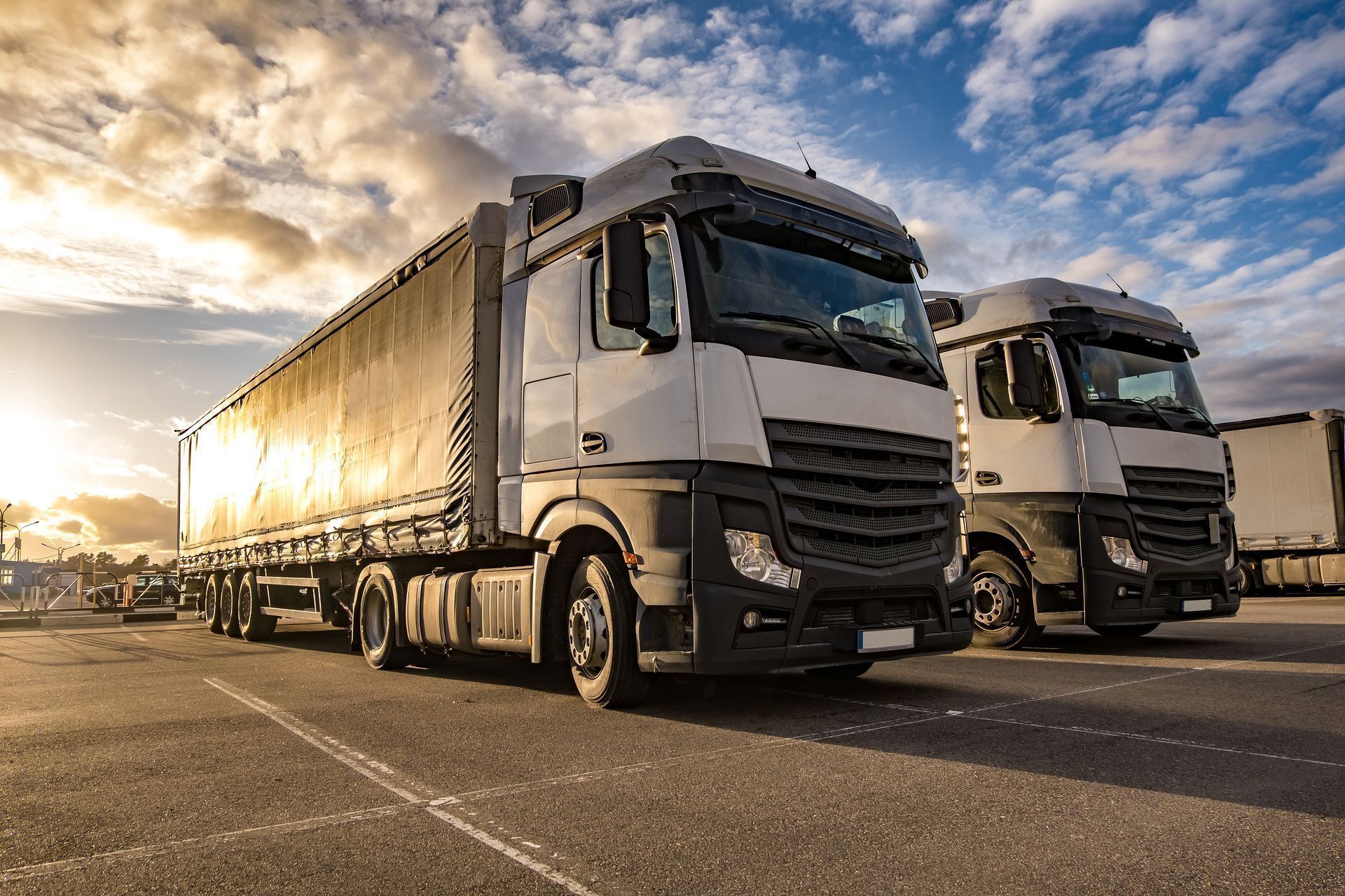 Two white cargo trucks parked on a road at sunset