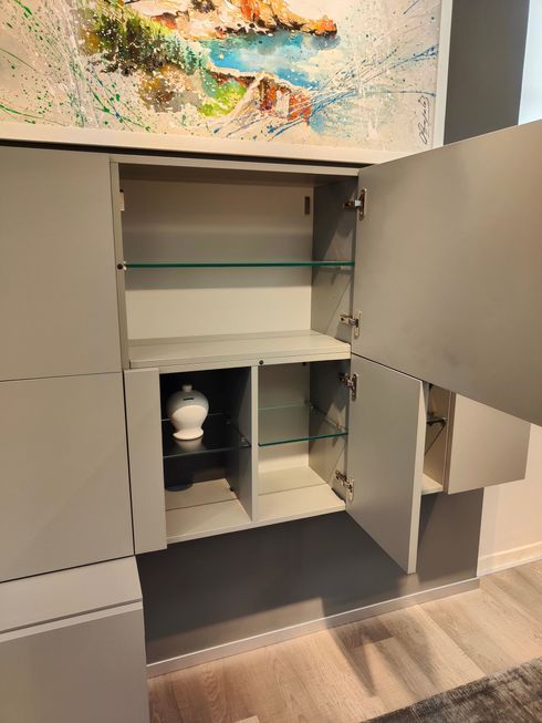 Un mobile bianco con le ante aperte e un quadro sulla parete dietro.