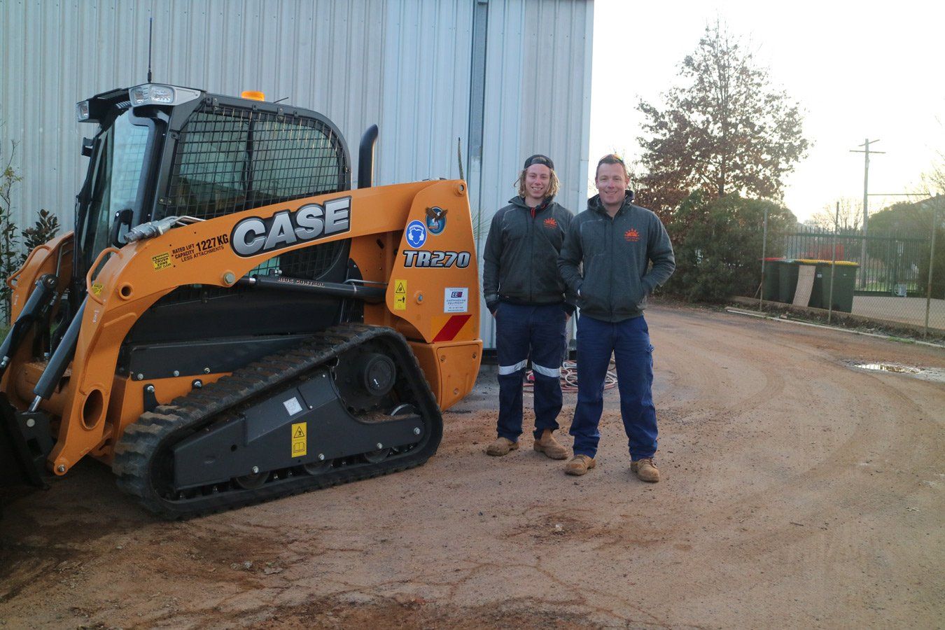 2 person posing together beside a machine