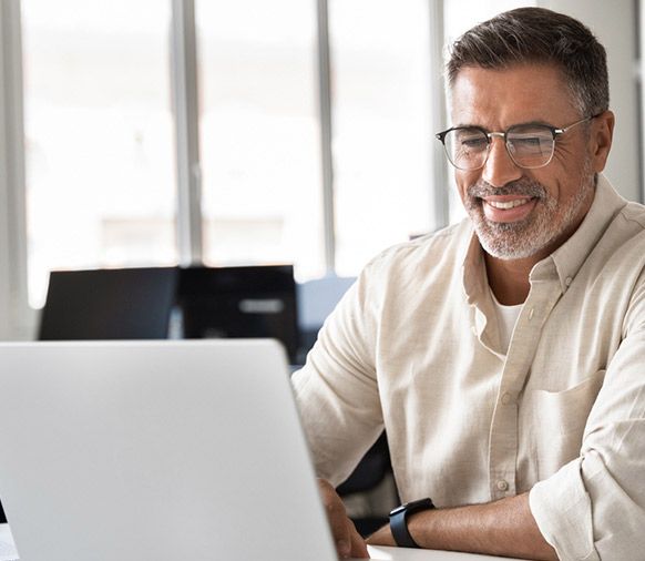 Um homem usando óculos sorri enquanto usa um laptop.