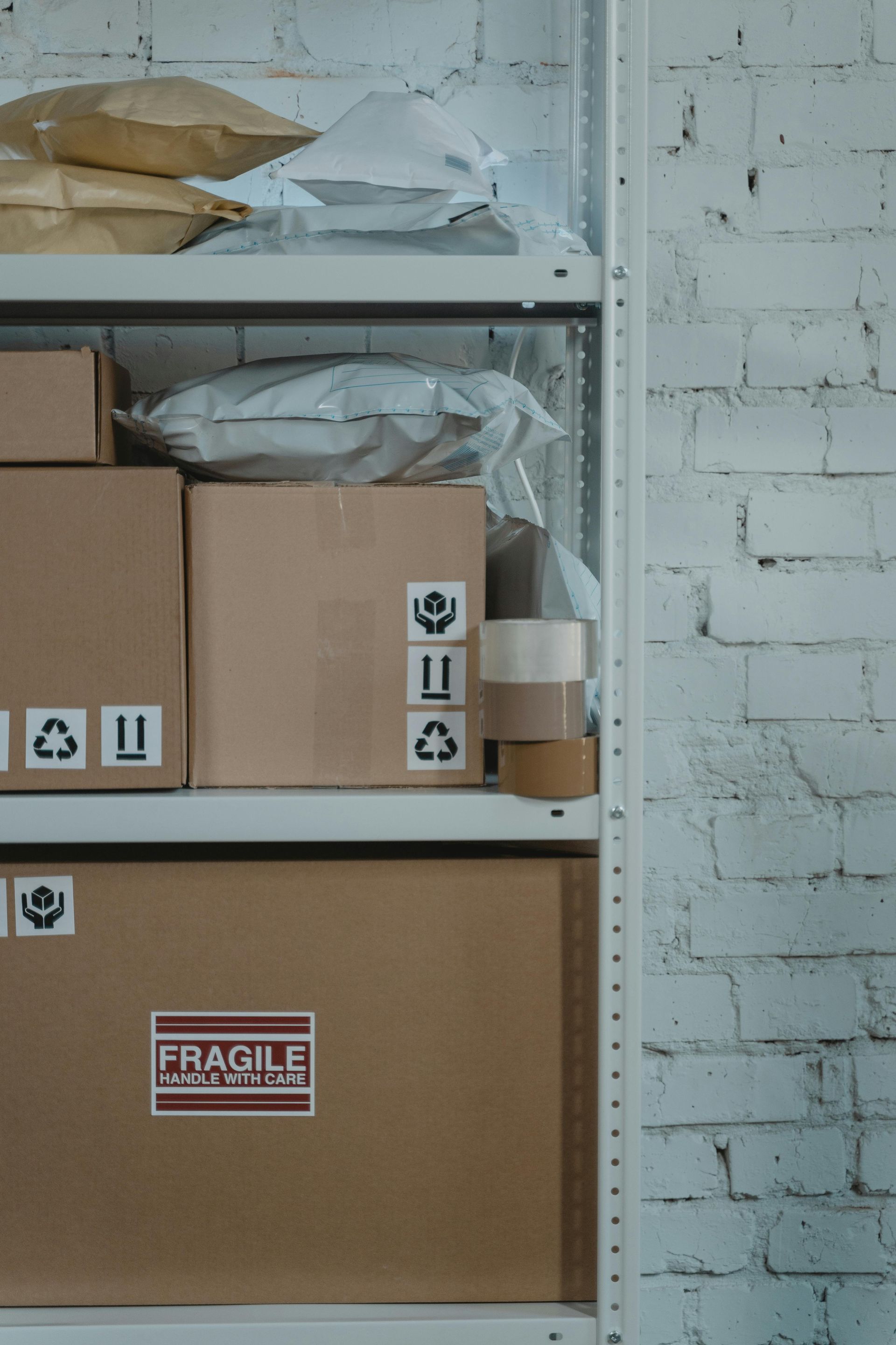 Cardboard boxes and packages on shelves against a white brick wall.