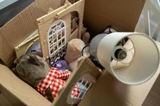 Cardboard box filled with toy house pieces, plush animals, and a lampshade.