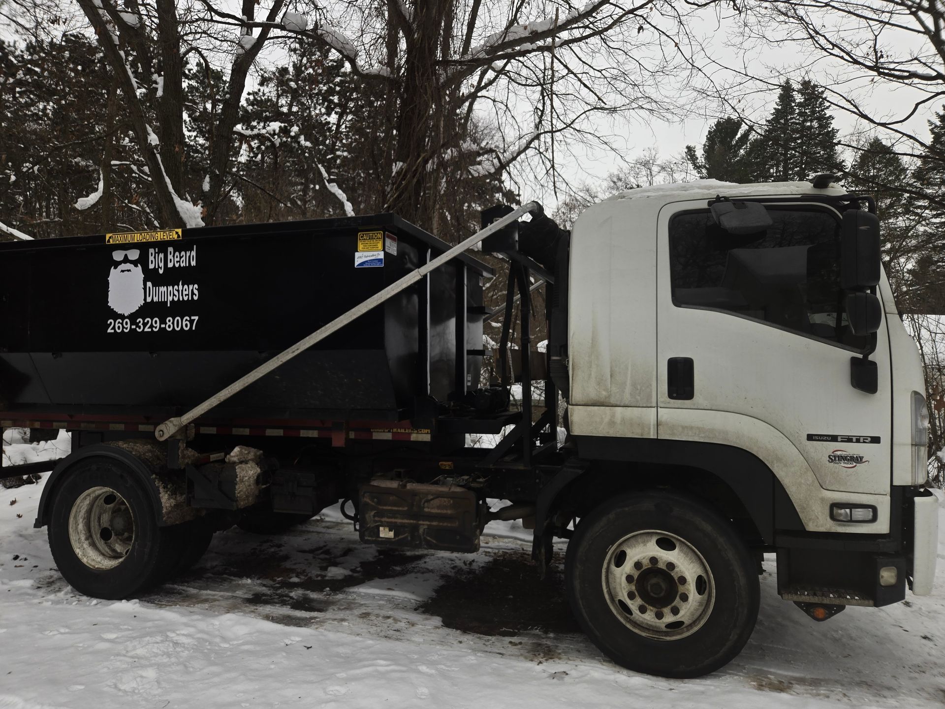 Black dumpster on a white truck in a snowy area.