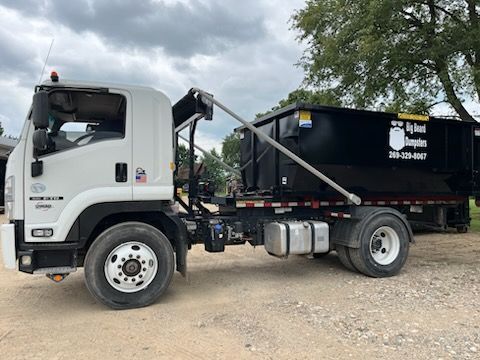 A dumpster truck is parked next to a dumpster.