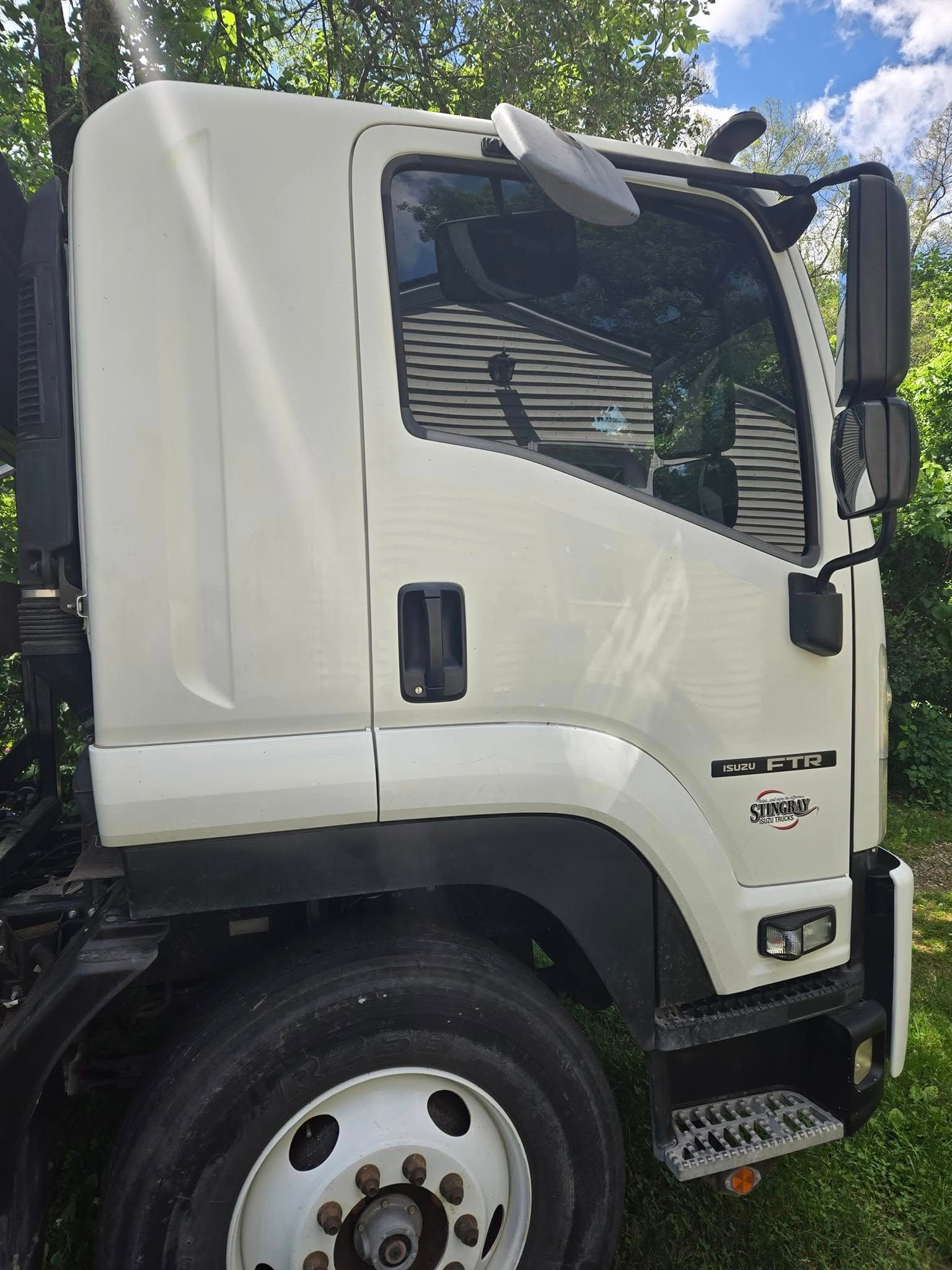 A white truck is parked in the grass next to trees.