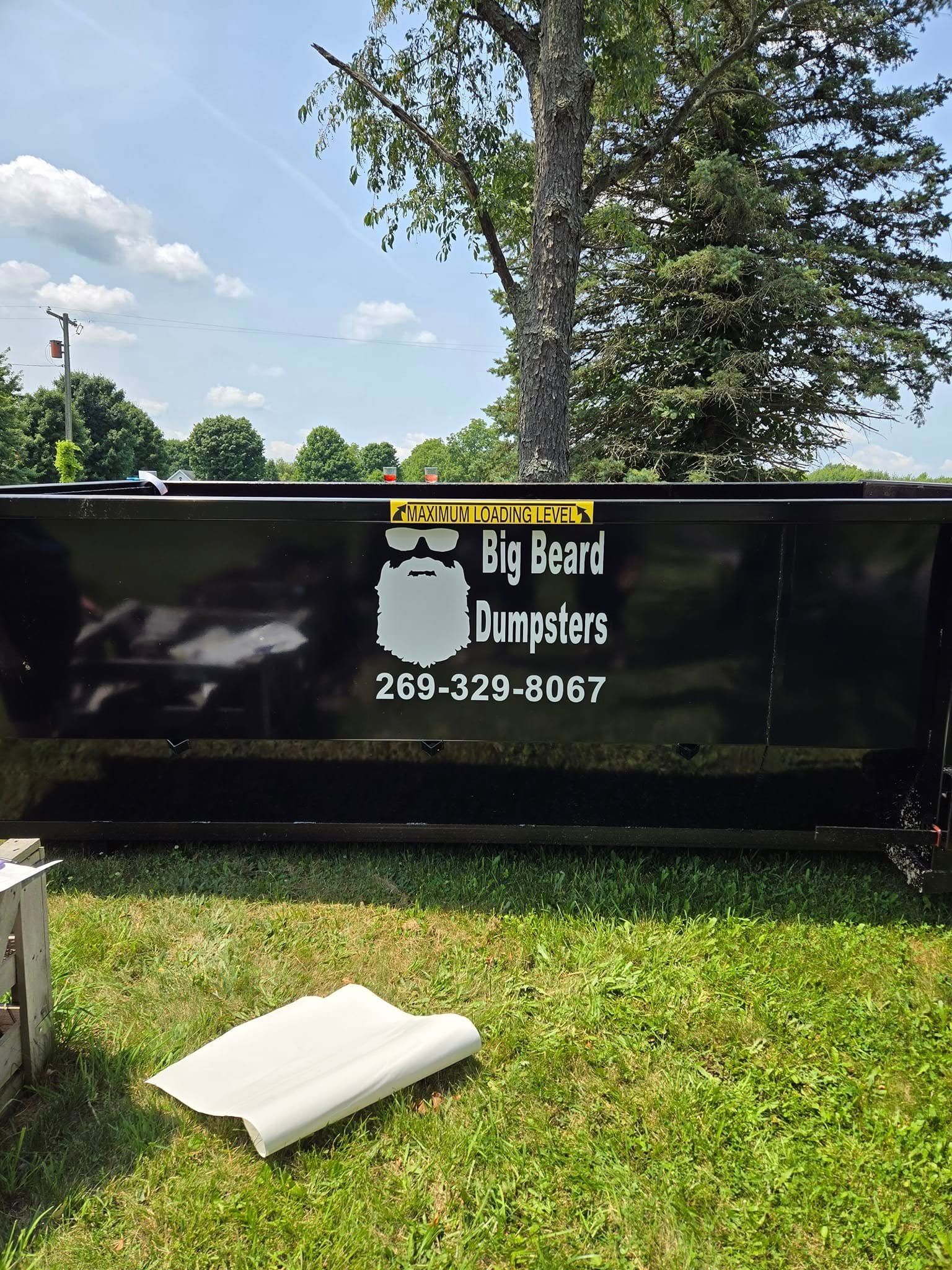 A black dumpster is sitting on top of a lush green field.
