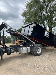 A dump truck with a dumpster attached to it is parked in a dirt lot.