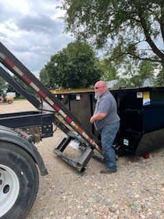 A man is loading a dumpster into a dump truck.
