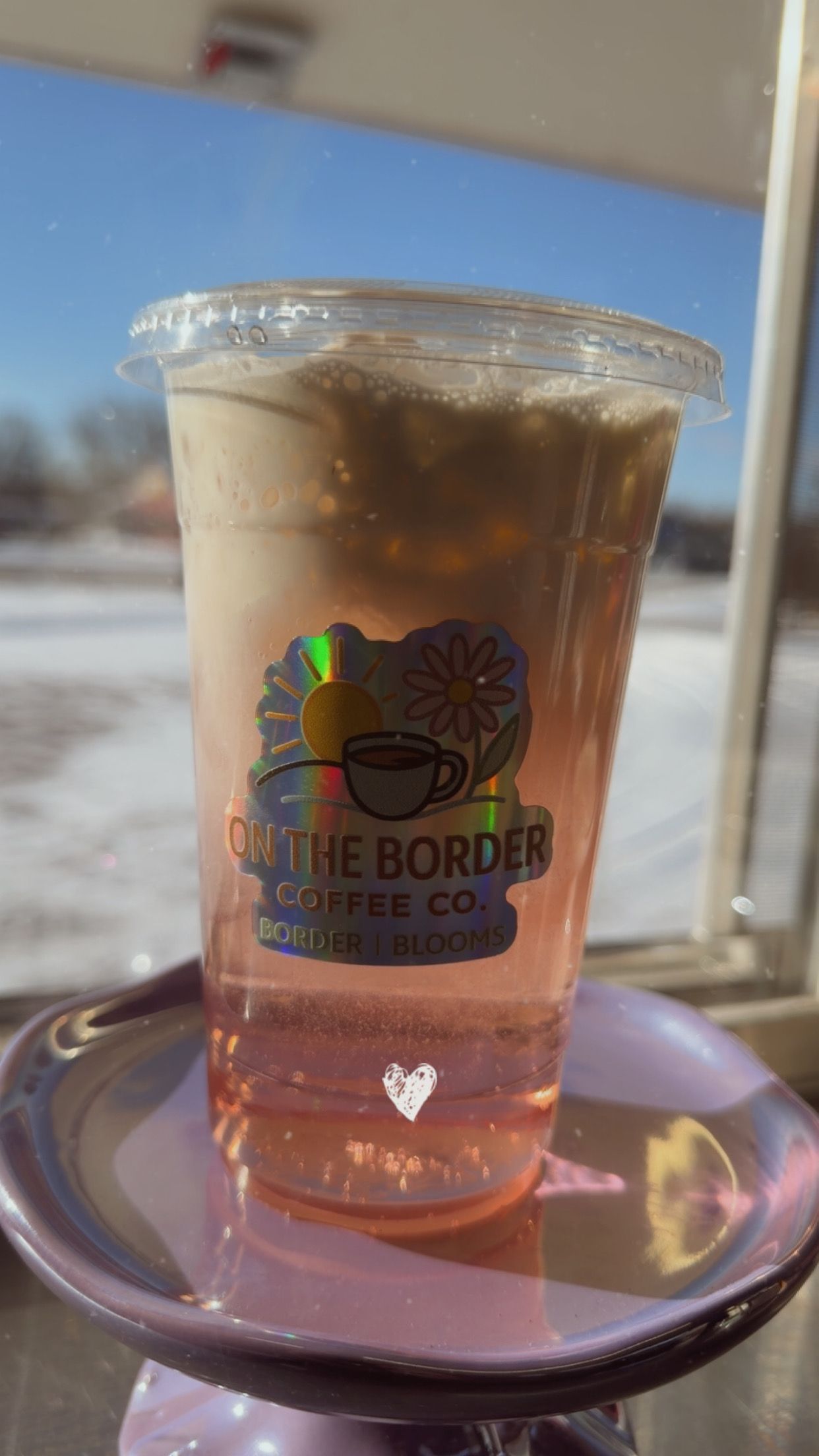 Iced pink drink with foam in a clear cup, sitting on a purple holder, with 