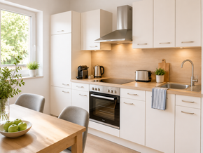 Helle, moderne Küche mit weißen Schränken, Edelstahlgeräten, Holztisch und einem Fenster mit Blick ins Grüne