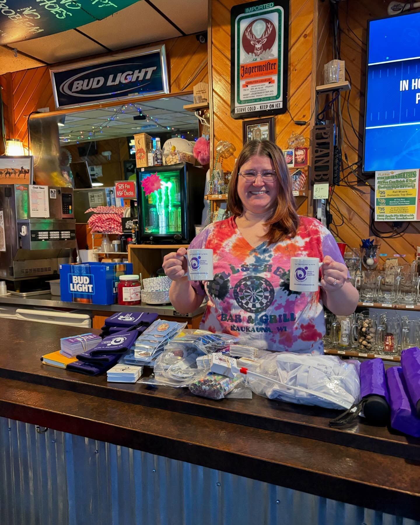 A woman is standing behind a bar holding two mugs.