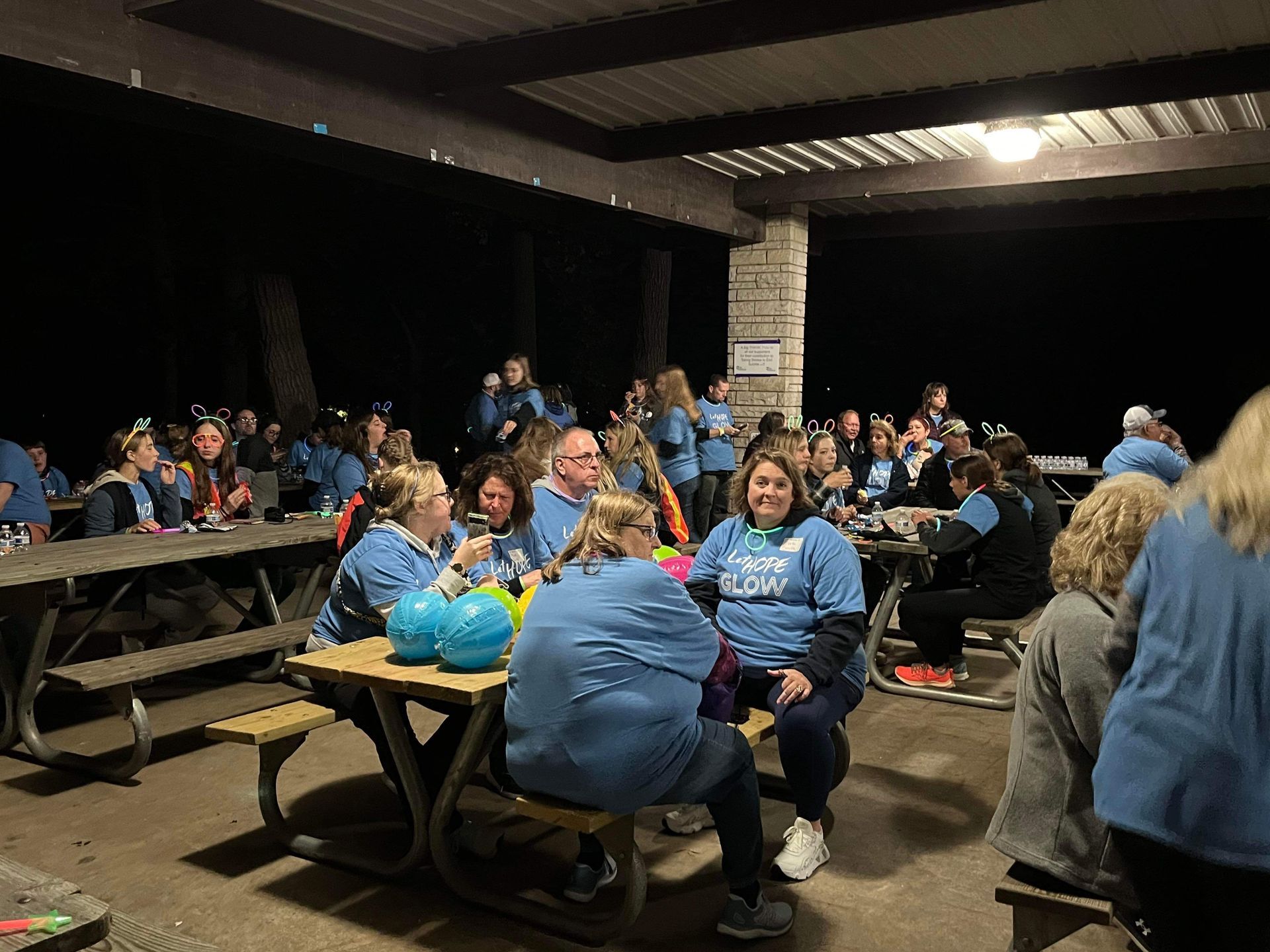 A group of people are sitting at picnic tables under a covered area.