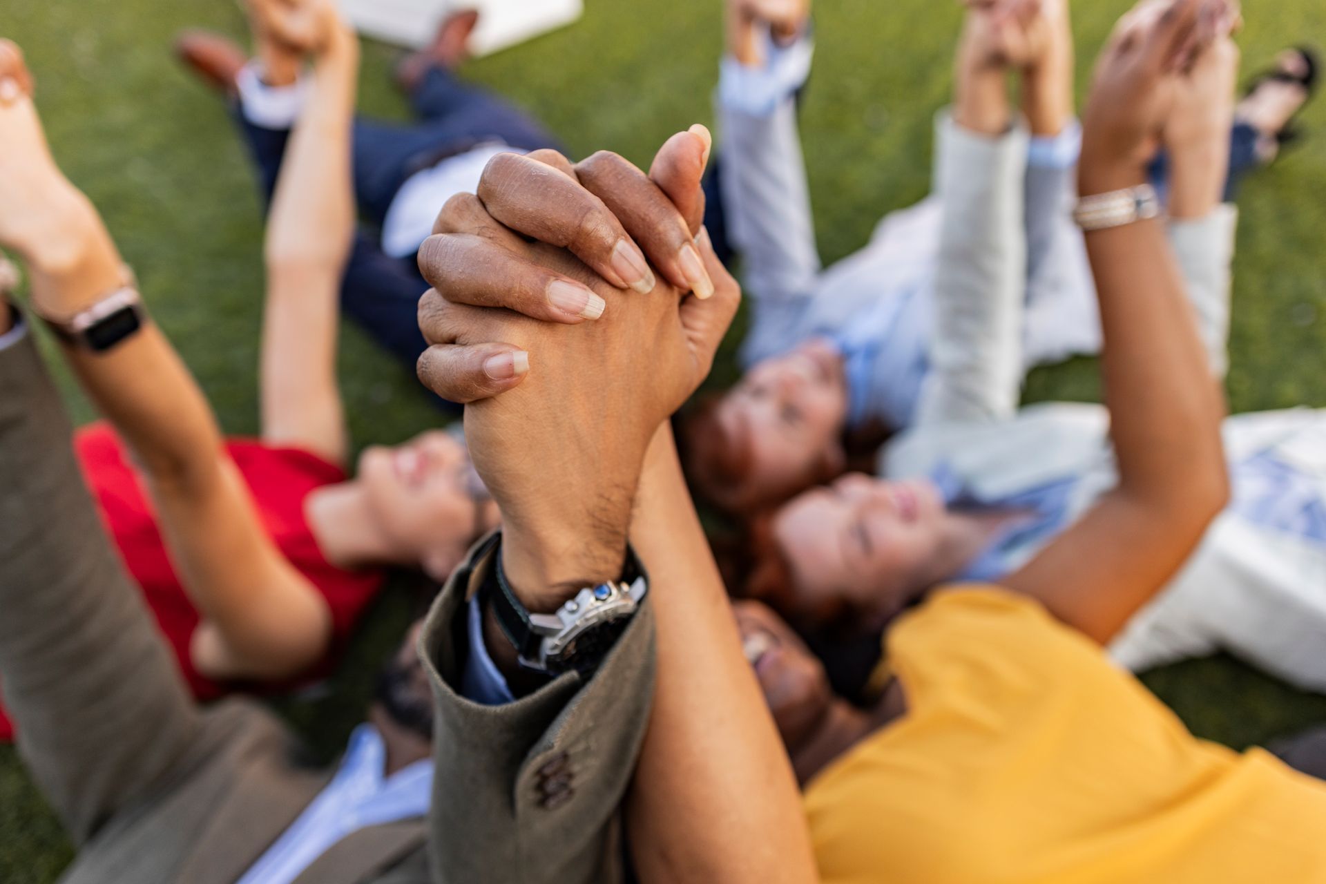 A group of people are laying on the grass holding hands.