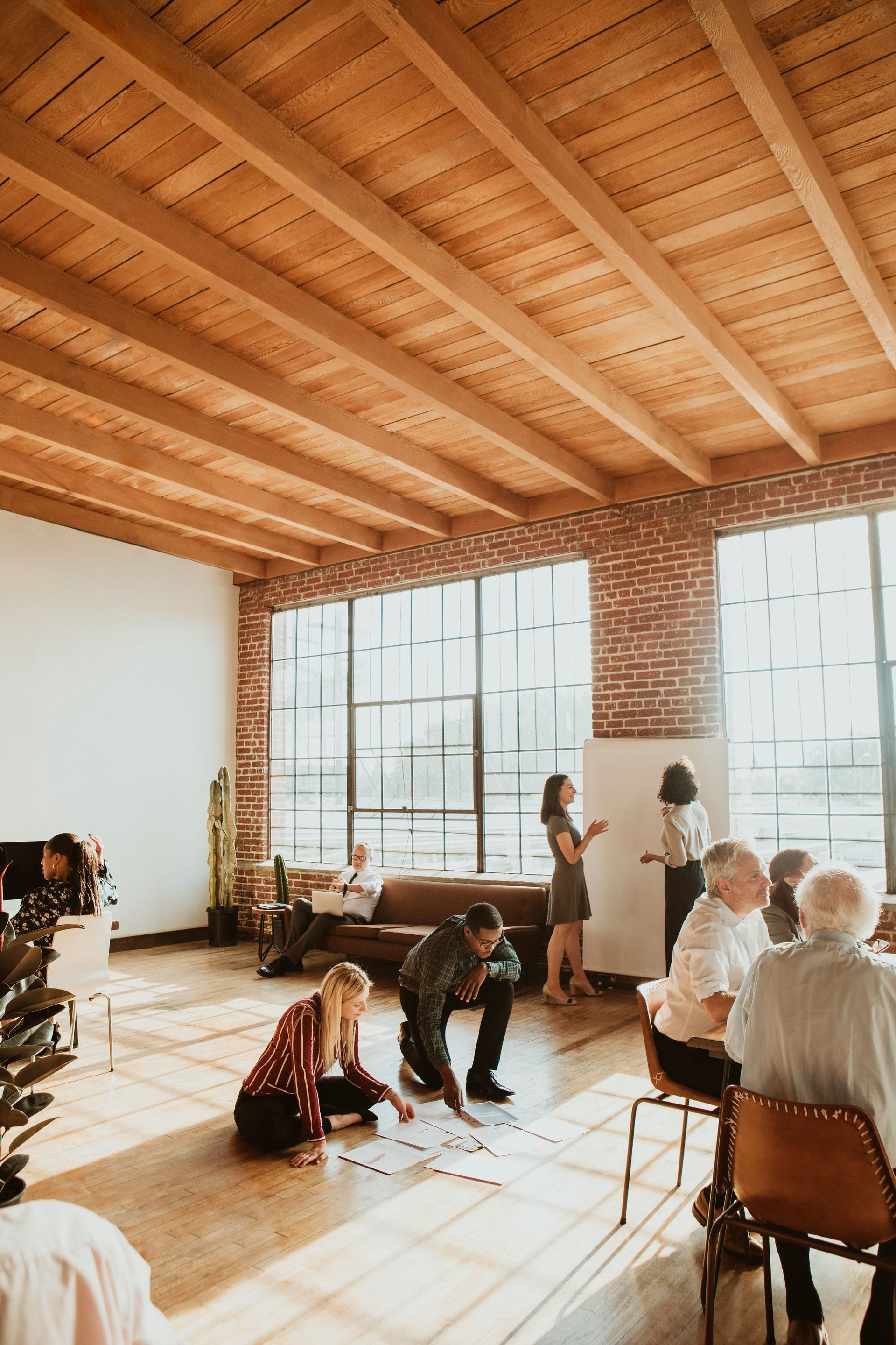 A group of people are sitting in a large room with a wooden ceiling.